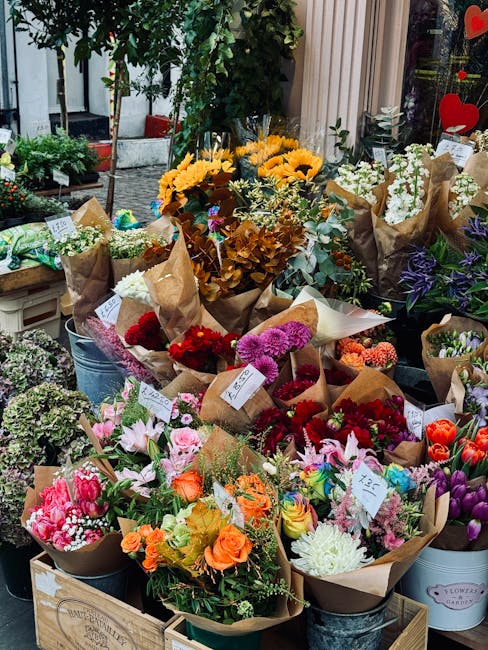 A vibrant display of fresh flower bouquets arranged outdoors in buckets and wooden crates at a flower shop near Canada Water station. The bouquets feature a variety of flowers including bright yellow 