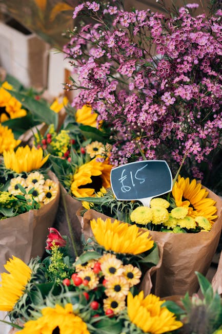 A vibrant display of fresh floral arrangements at a market stand, showcasing a variety of flowers including bright yellow sunflowers, small white daisy-like blooms with yellow centers, and clusters of
